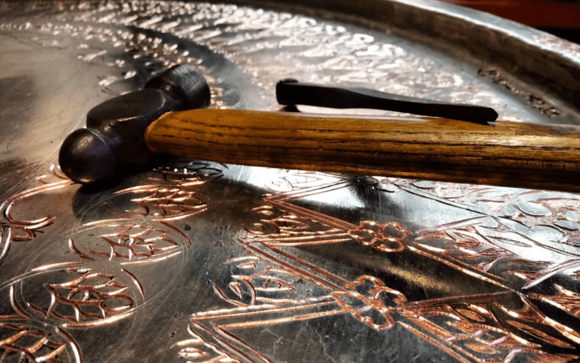Coppersmith hammer resting on an engraved copper tray